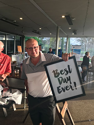 man holds "Best Day Ever!" sign at a Golf Day to raise Epilepsy Awareness
